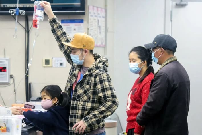 Un familiar (2º por la izquierda) sostiene un gotero intravenoso para una niña (izquierda) que recibe atención en el departamento de pediatría de un hospital de Hangzhou, en la provincia de Zhejiang, al este de China, el 6 de enero de 2025. (AFP/China)