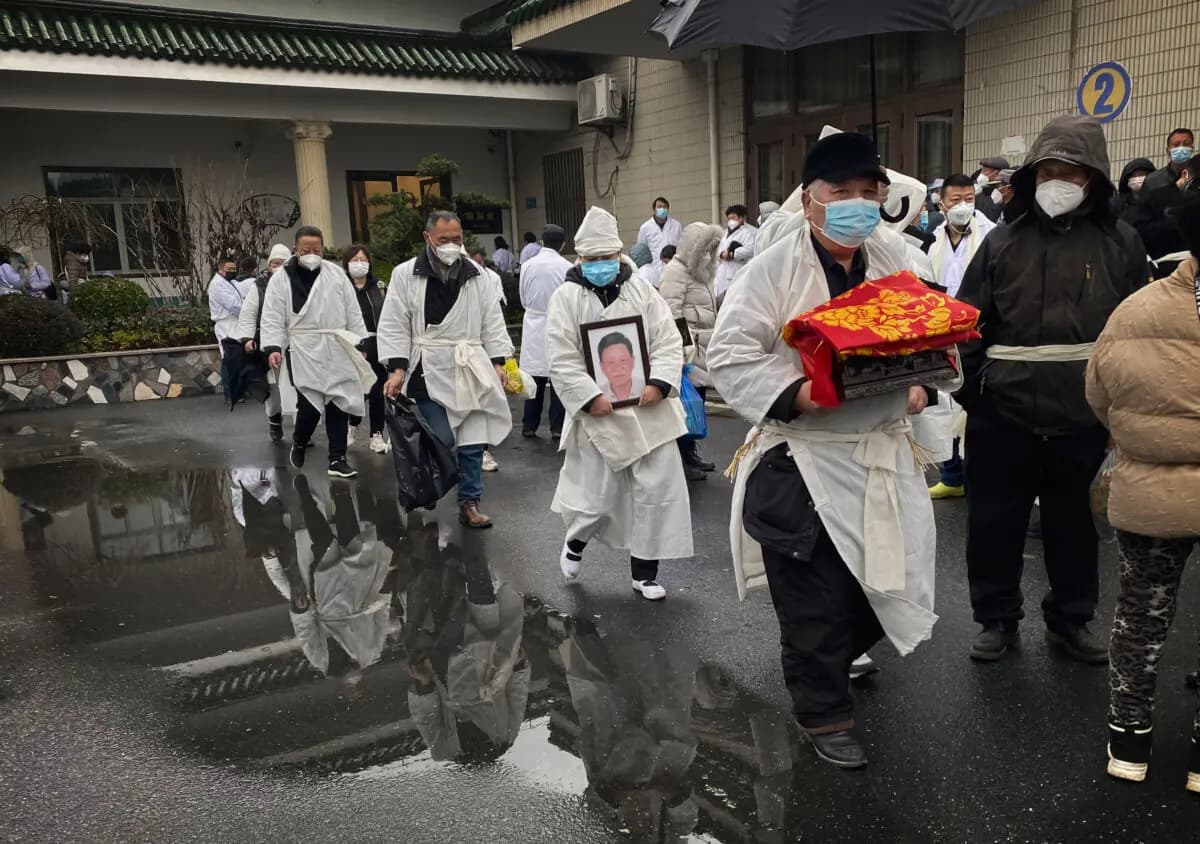 Un doliente lleva los restos incinerados de un ser querido mientras él y otros visten la tradicional ropa blanca de funeral, durante un funeral en Shanghái, China, el 14 de enero de 2023. (Kevin Frayer/Getty Images)