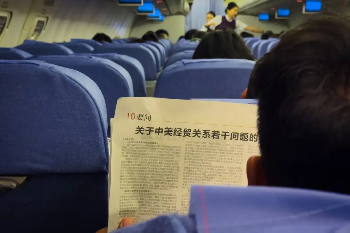 Un pasajero lee un artículo de prensa titulado «La posición de China sobre varias cuestiones relativas a las relaciones económicas y comerciales entre China y Estados Unidos», que forma parte de un libro blanco publicado por la Oficina de Información del Consejo de Estado de China el 9 de abril, a bordo de un vuelo comercial de Chongqing a Shenzhen, con la tripulación de cabina trabajando en segundo plano, en Shenzhen, China, el 10 de abril de 2025. (Cheng Xin/Getty Images)