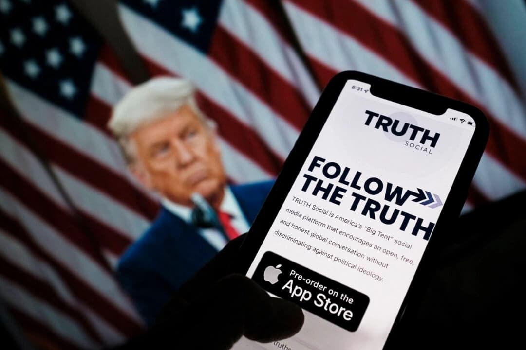 Esta foto ilustrativa muestra a una persona consultando la tienda de aplicaciones de un smartphone en busca de Truth Social, con una foto del expresidente Donald Trump en la pantalla de un ordenador al fondo, en Los Ángeles, el 20 de octubre de 2021. (Chris Delmas/AFP a través de Getty Images)