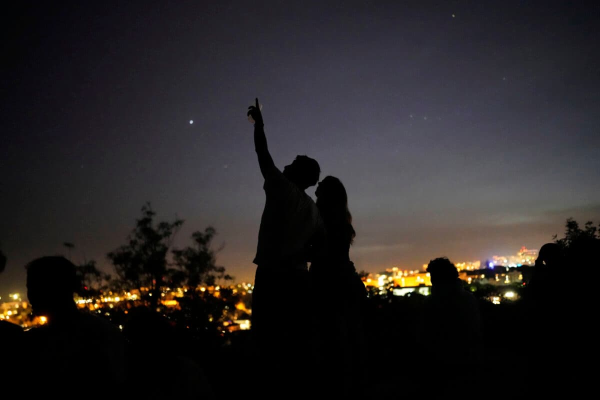 Una joven pareja se encuentra de pie sobre un muro mirando al cielo en un mirador con vistas a Lisboa durante un apagón nacional, el 28 de abril de 2025. (Armando Franca/AP Photo).