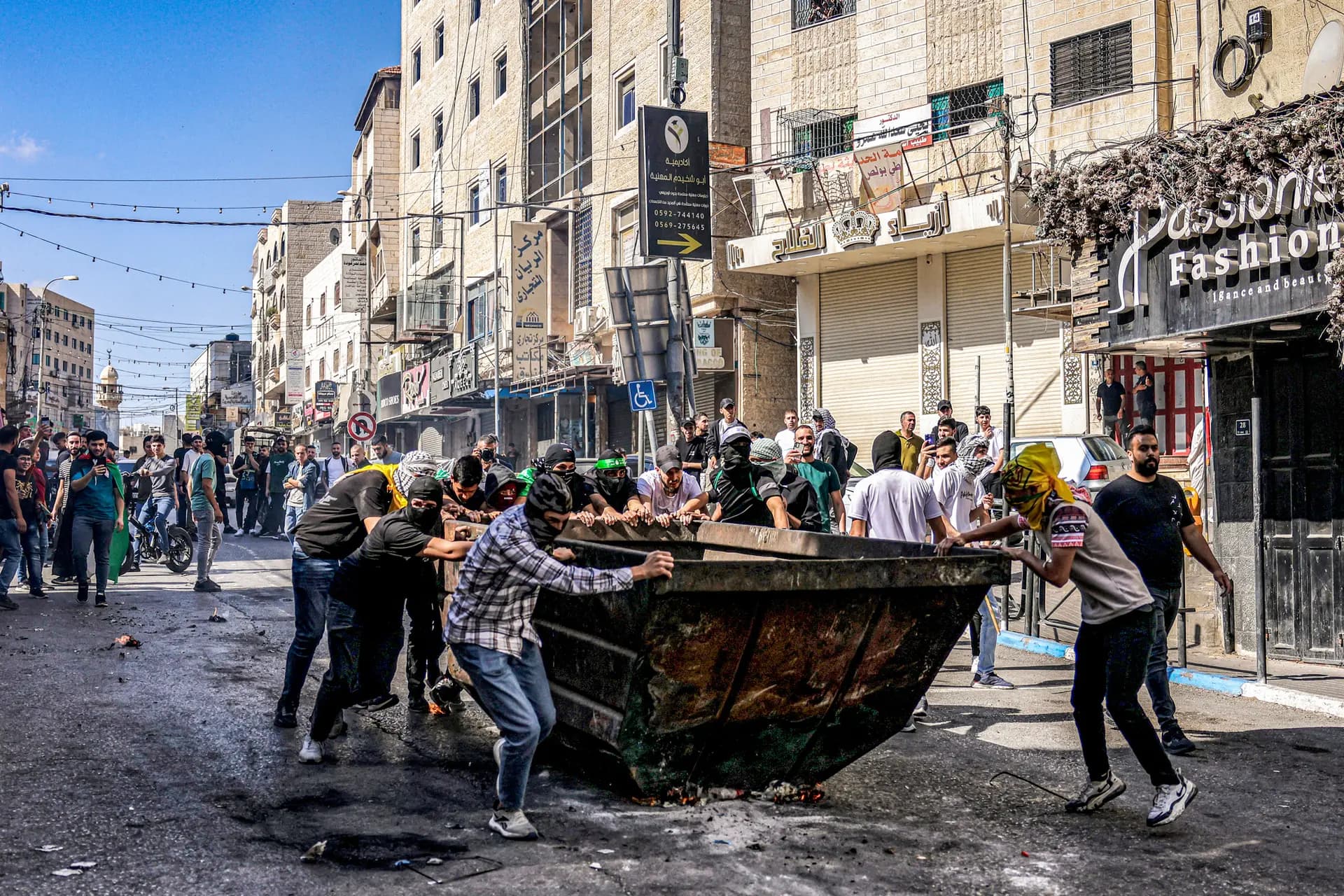 <em>Manifestantes palestinos empujan un contenedor de basura para protegerse durante enfrentamientos con las fuerzas israelíes tras una manifestación en apoyo a Gaza en Hebrón, Cisjordania, el 13 de octubre de 2023. La Corte Suprema está considerando dos casos sobre si las familias de las víctimas de atentados terroristas pueden demandar a la Organización para la Liberación de Palestina (OLP). Hazem Bader/AFP vía Getty Images</em>