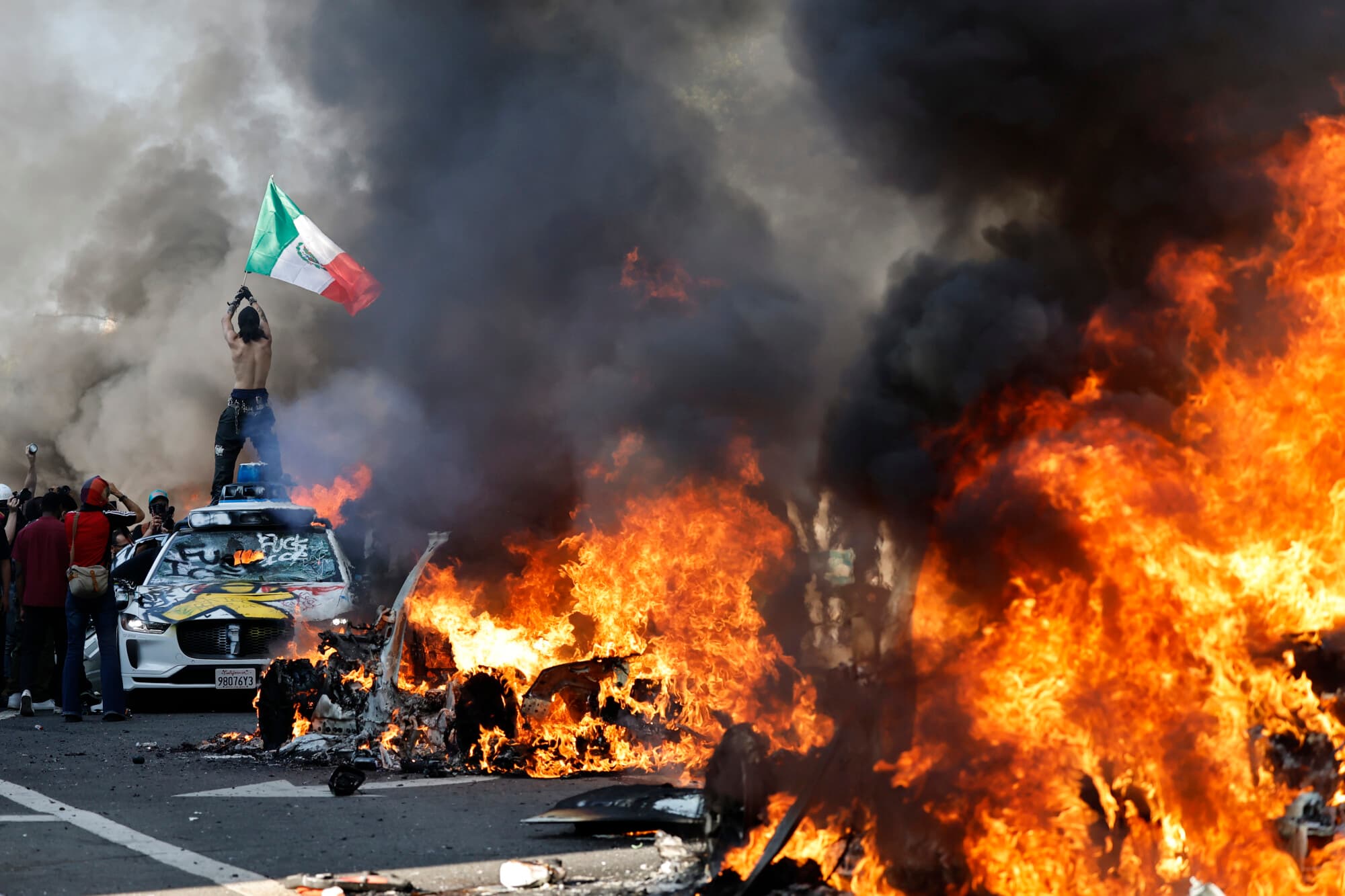 Un manifestante sostiene una bandera mexicana mientras carros en llamas se alinean en la calle el 8 de junio de 2025 en Los Ángeles, California. (Foto de Mario Tama/Getty Images)