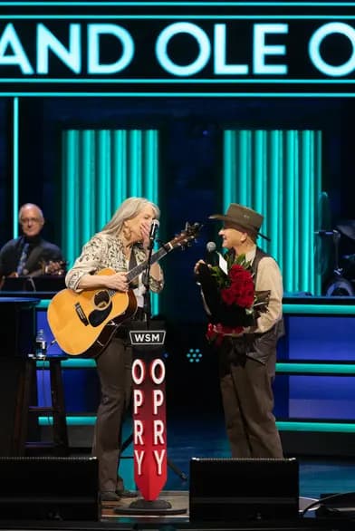 Kathy Mattea recibe una sorpresa en el escenario cuando el miembro del Opry, Charlie McCoy, la invita a formar parte del Grand Ole Opry. (Cortesía del Grand Ole Opry)