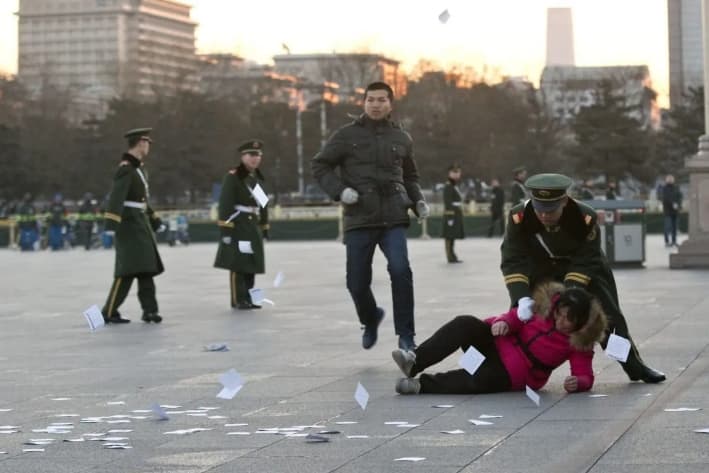 Una demandante es empujada al suelo por un policía paramilitar después de correr hacia una zona acordonada cerca de un mástil con la bandera nacional en la plaza de Tiananmen y lanzar panfletos para protestar por su caso de injusticia, en Beijing, el 5 de marzo de 2014. (Alexander F. Yuan /AP Photo)