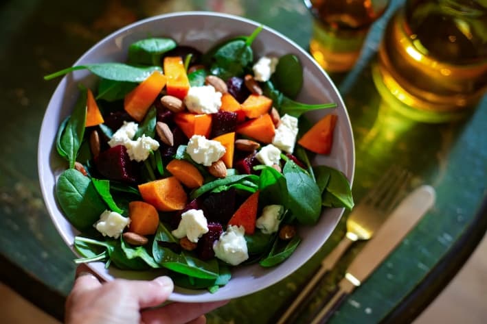 Un bol de ensalada de espinacas con kaki, remolacha, almendras y queso gorgonzola. El folato, o vitamina B9, se obtiene de alimentos como las espinacas y los frutos secos. Las autoridades afirmaron que la leucovorina, o ácido folínico recetado, puede ayudar a las personas autistas con sus síntomas. (Kathrin Ziegler/Getty Images)