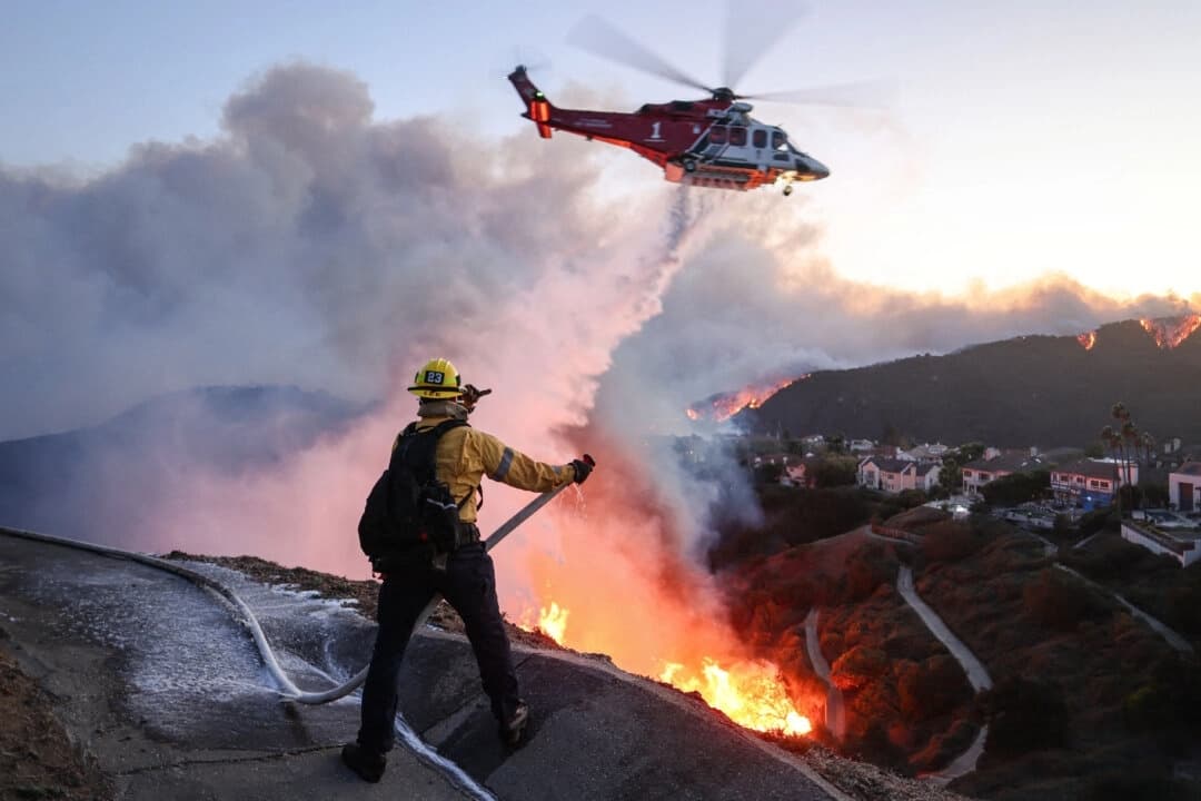 El personal de bomberos responde a los hogares destruidos mientras un helicóptero lanza agua a medida que el incendio Palisades crece en Pacific Palisades, California, el 7 de enero de 2025. (David Swanson/AFP vía Getty Images)
