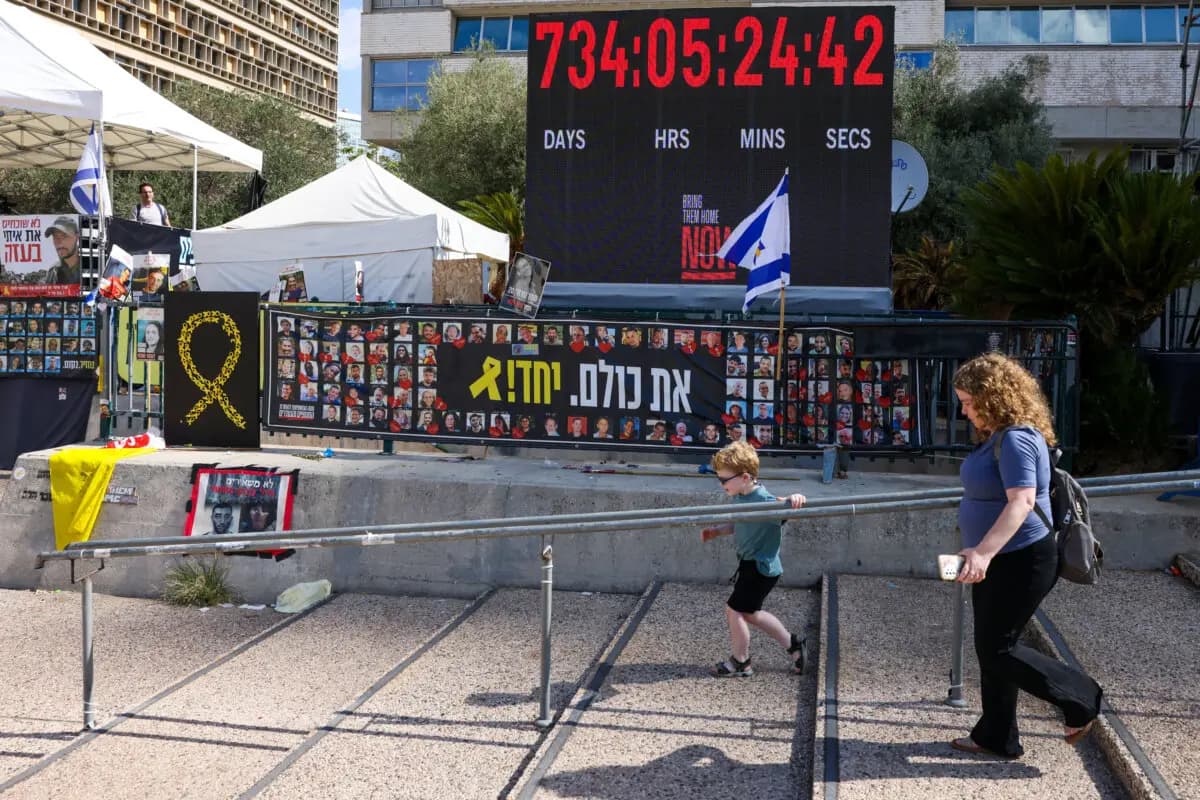 <em>Una mujer y un niño caminan junto a carteles de rehenes retenidos por Hamás en Gaza, en la Plaza de los Rehenes de Tel Aviv, el 10 de octubre de 2025. (Ahmad Gharabli/AFP vía Getty Images)</em>