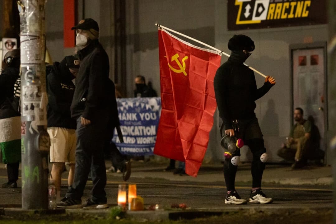 Una mujer lleva una bandera comunista frente a las oficinas del Servicio de Inmigración y Control de Aduanas en Portland, Oregón, el 4 de octubre de 2025. (John Fredricks/The Epoch Times)