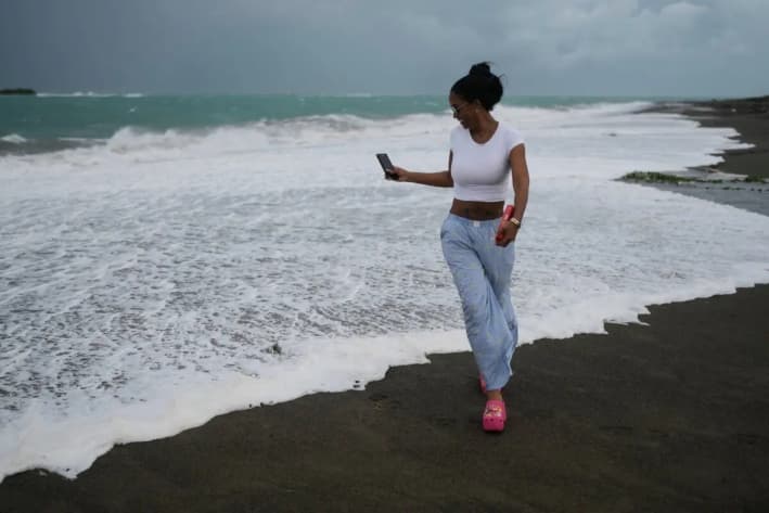 Una mujer pasea por la playa antes de la llegada prevista del huracán Melissa a Kingston, Jamaica, el 26 de octubre de 2025. (AP Photo/Matias Delacroix)