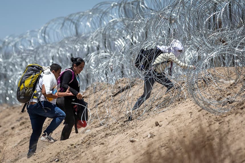 Inmigrantes caminan entre alambradas que rodean un campamento improvisado para migrantes tras cruzar la frontera desde México el 11 de mayo de 2023 en El Paso, Texas. (John Moore/Getty Images)