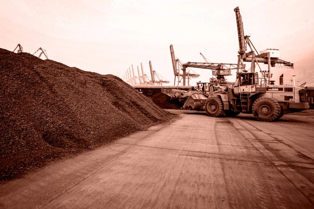 <em>Un hombre conduce una pala cargadora frontal para extraer tierra que contiene minerales de tierras raras para su exportación a Japón en un puerto de Lianyungang, provincia de Jiangsu, China, el 5 de septiembre de 2010. China ostenta un cuasi monopolio sobre la industria de las tierras raras, desde la minería y el refinado hasta la fabricación de imanes. (Editado por The Epoch Times, STR/AFP vía Getty Images)</em>
