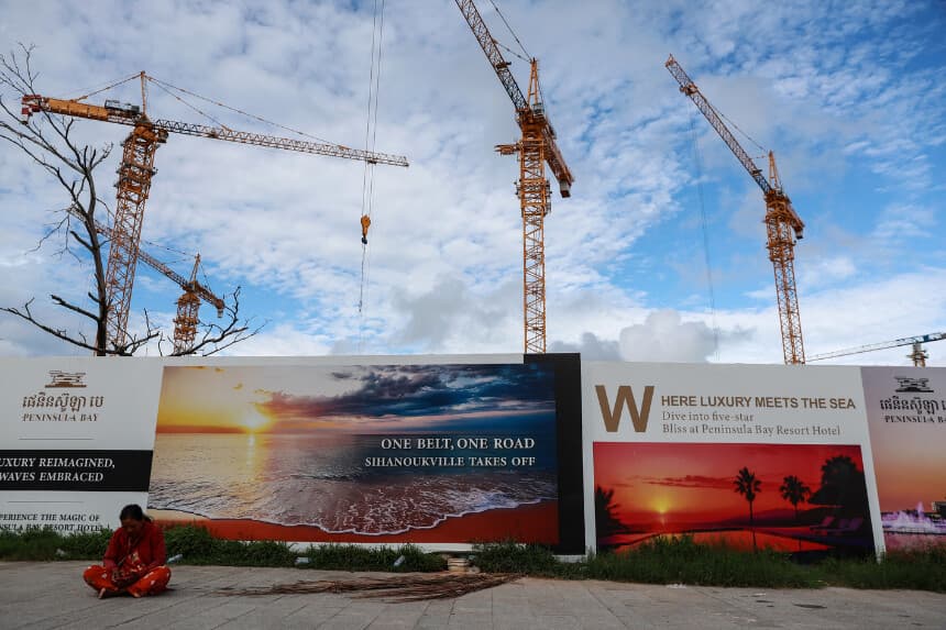 Una mujer sentada cerca de una valla publicitaria de la iniciativa china "El cinturón y la ruta" el 1 de julio de 2024 en Sihanoukville, Camboya. (Valeria Mongelli/Getty Images)