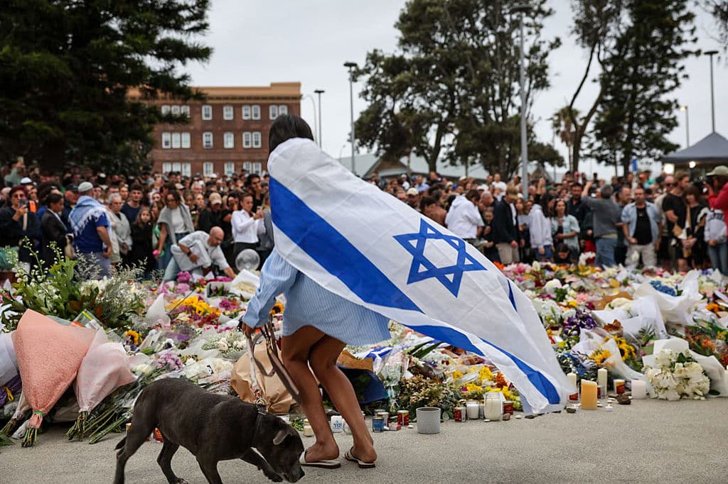 Una persona vestida con una bandera israelí deposita flores en la playa de Bondi, el 15 de diciembre de 2025, en Sídney, Australia. (Izhar Khan/Getty Images)