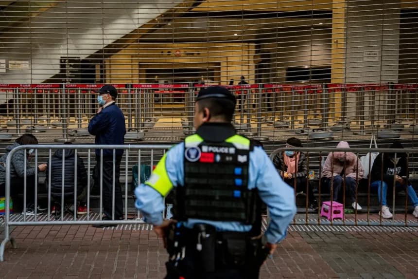 Un agente de policía vigila mientras la gente espera en fila para entrar en el edificio de los tribunales de West Kowloon para escuchar los veredictos del juicio por seguridad nacional contra el magnate de los medios de comunicación prodemocráticos Jimmy Lai, en Hong Kong, el 15 de diciembre de 2025. (Leung Man Hei/AFP a través de Getty Images)
