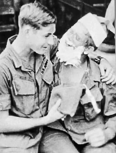 Tim Connaghan (derecha) posa como Papá Noel mientras estaba destinado en Vietnam el 23 de diciembre de 1969. Se puso el traje por primera vez para repartir bolsas de regalos navideños de la Cruz Roja y, desde entonces, ha pasado más de 50 años perfeccionando el papel. (Cortesía de Tim Connaghan)
