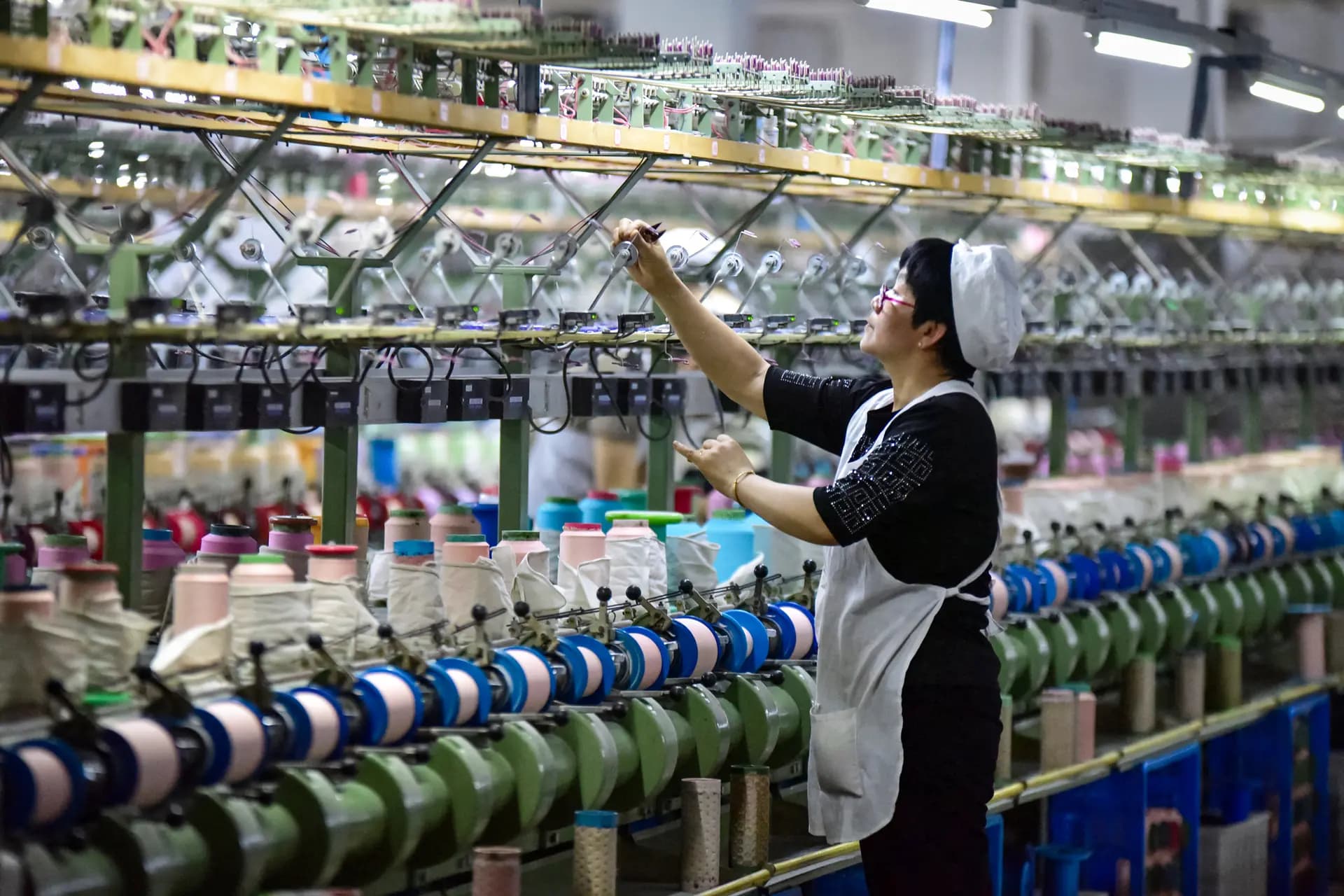 Un trabajador revisa una máquina en una fábrica de tejidos de seda en Fuyang, provincia de Anhui, China, el 16 de abril de 2025. El economista Davy J. Wong dijo que el problema más profundo de la evasión arancelaria en China tiene que ver con los productos intermedios chinos utilizados en la producción en terceros países, insumos que describió como "legales, estructurales y más difíciles de controlar". (STR/AFP a través de Getty Images).