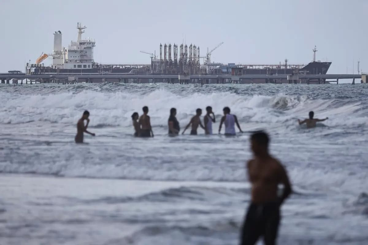 Personas caminan por una playa frente a un petrolero anclado en el muelle cerca de la refinería El Palito, en Puerto Cabello, Venezuela, el 18 de diciembre de 2025. (Jesús Vargas/Getty Images)