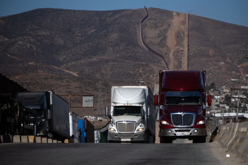 Camiones de carga hacen fila junto al muro fronterizo antes de cruzar hacia los Estados Unidos en el puerto comercial de Otay en Tijuana, estado de Baja California, México, el 31 de julio de 2025.(GUILLERMO ARIAS/AFP via Getty Images)