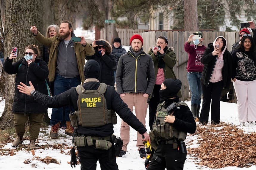 Observadores graban a agentes del ICE mientras mantienen un perímetro de seguridad luego de que uno de sus vehículos sufriera un pinchazo en Penn Avenue, el 5 de febrero de 2026, en Minneapolis, Minnesota. (Stephen Maturen/Getty Images)