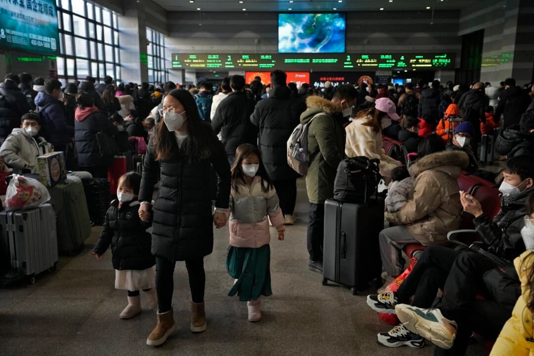 Una mujer y unos niños con mascarillas caminan junto a viajeros enmascarados que esperan en la sala de salidas para coger sus trenes en la estación ferroviaria oeste de Beijing el 15 de enero de 2023. (Andy Wong/AP Photo)