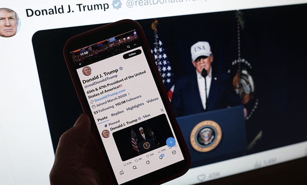 <em>Esta imagen ilustrativa muestra a una persona mirando un teléfono inteligente que muestra al presidente estadounidense Donald Trump haciendo una declaración sobre las operaciones de combate en Irán, junto a una pantalla de computadora con el mismo mensaje publicado el 28 de febrero de 2026 en X. (Foto de Chris DELMAS / AFP vía Getty Images)</em>