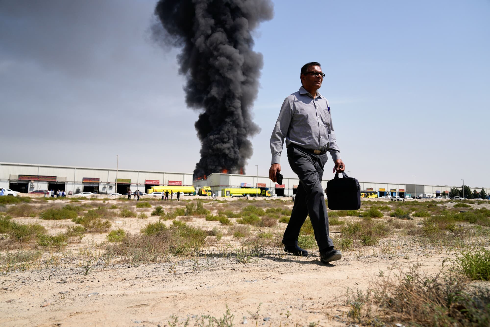 Un hombre se aleja mientras una columna de humo negro se eleva desde un almacén en la zona industrial de la ciudad de Sharjah, Emiratos Árabes Unidos, tras las noticias de ataques iraníes en Dubái el 1 de marzo de 2026. (AP Photo/Altaf Qadri)