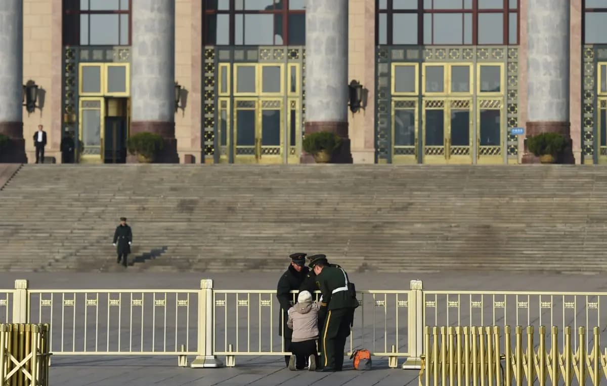 Oficiales de la policía paramilitar detienen a una mujer mientras protesta de rodillas frente al Gran Salón del Pueblo durante una sesión anual de la legislatura china, la Asamblea Popular Nacional, en Beijing, el 13 de marzo de 2015. (Greg Baker/AFP/Getty Images).