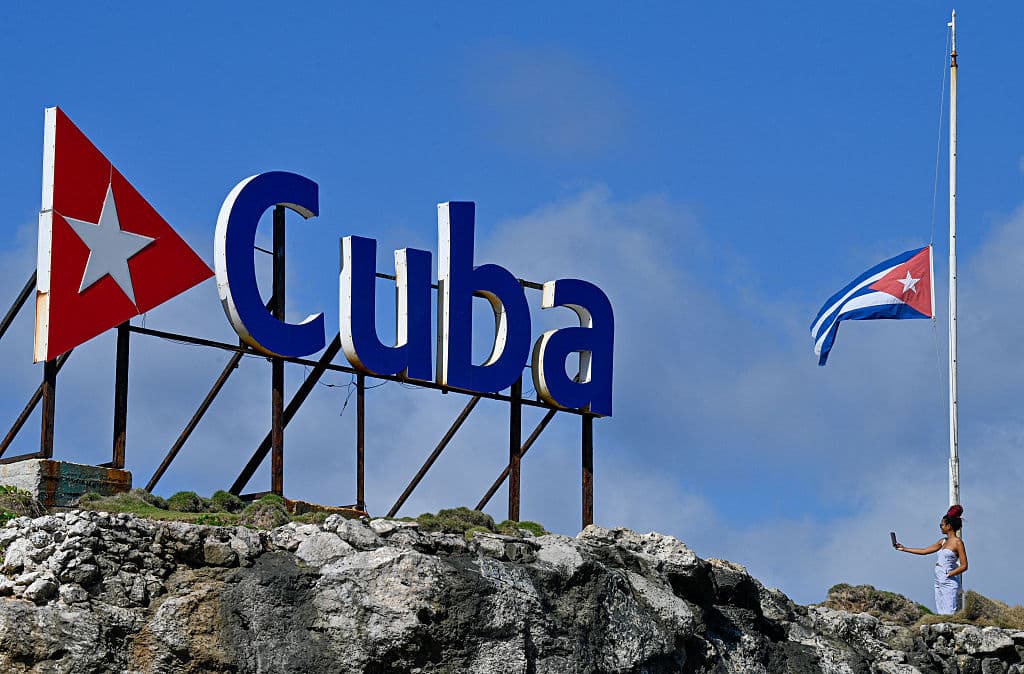 Mujer se toma una selfie junto a una bandera cubana a media asta en La Habana el 5 de enero de 2026. La Habana declaró dos días de duelo nacional a partir del 5 de enero tras la muerte de 32 cubanos durante el ataque estadounidense a Caracas que culminó con la captura del presidente venezolano, Nicolás Maduro. (Foto de Adalberto ROQUE / AFP vía Getty Images)
