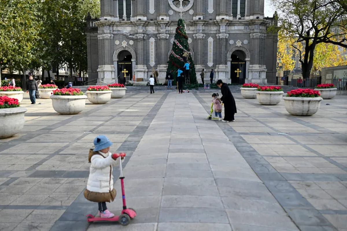 Trabajadores decoran un árbol de Navidad mientras unos niños juegan frente a una iglesia en Beijing el 28 de noviembre de 2025. (Wang Zhao/AFP).