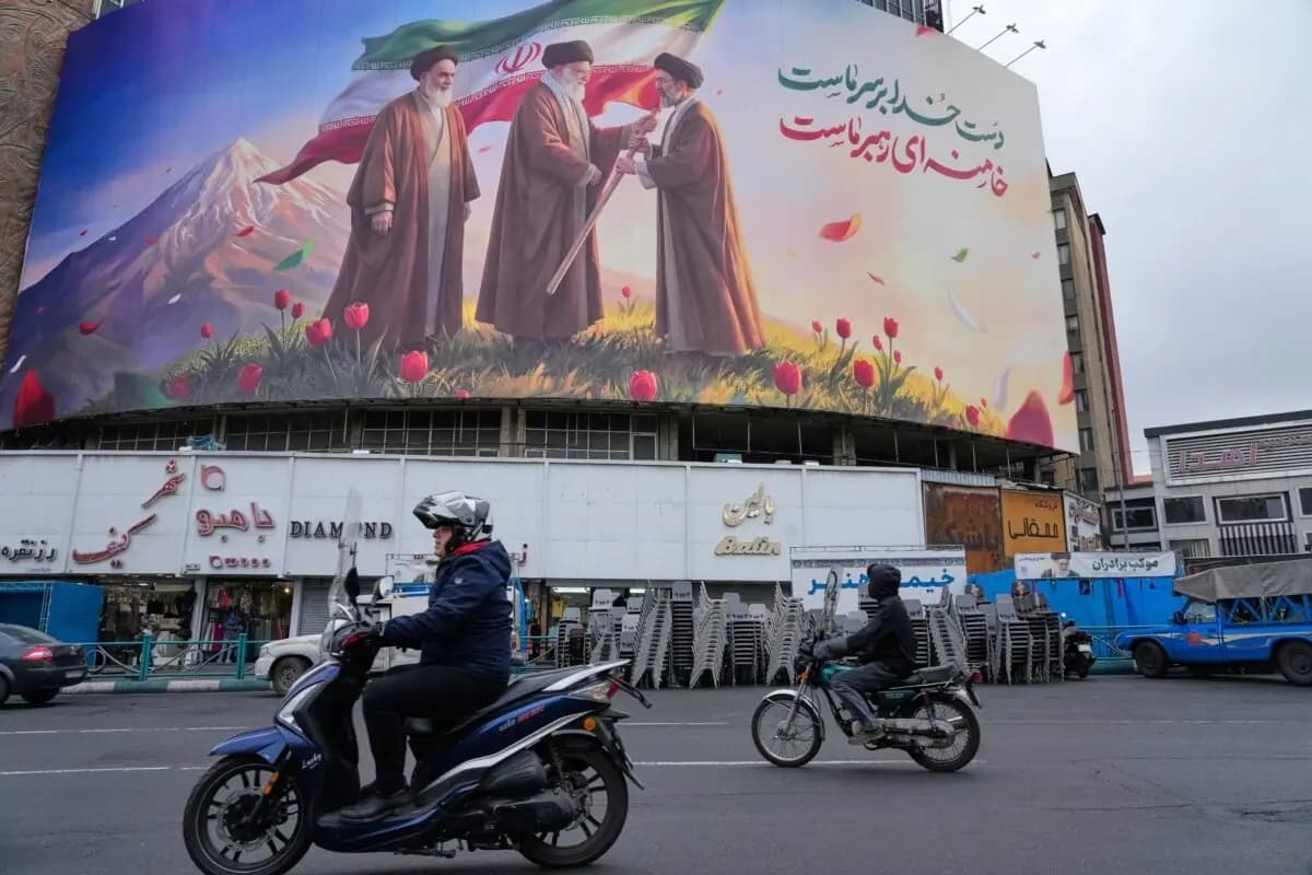 Unas motocicletas pasan junto a una valla publicitaria en la que se ve al difunto líder supremo de Irán, el ayatolá Ali Jamenei (C), entregando la bandera del país a su hijo y sucesor, el ayatolá Mojtaba Jamenei (D), mientras el difunto fundador de la revolución, el ayatolá Ruhollah Jomeini (I), observa, en una plaza del centro de Teherán, Irán, el 10 de marzo de 2026. (Vahid Salemi/AP Photo)
