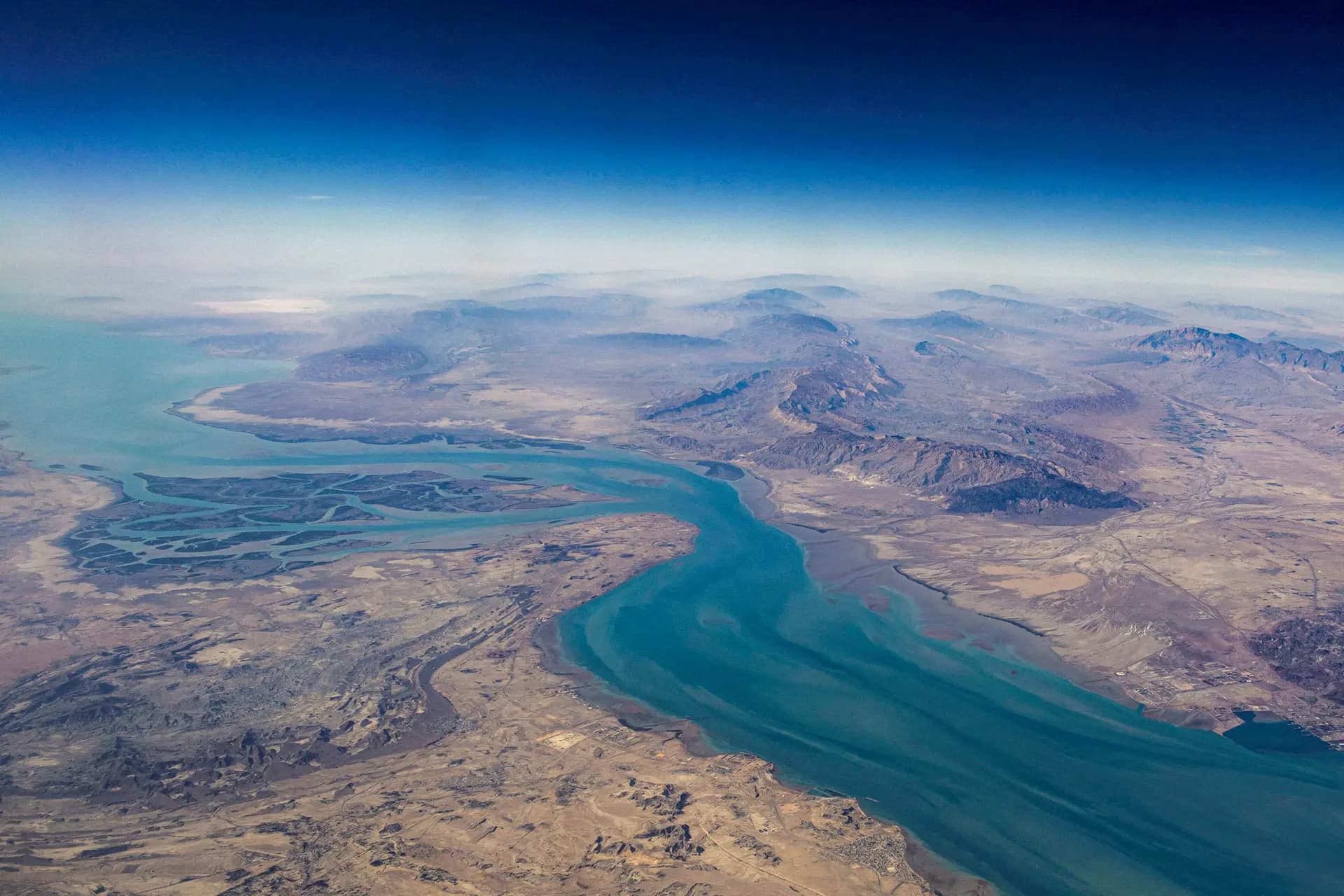 (Arriba) Buques cisterna navegan en el Golfo Pérsico, cerca del estrecho de Ormuz, en medio de la guerra entre Estados Unidos e Israel e Irán, vistos desde el norte de Ras al-Khaimah, cerca de la frontera con la gobernación de Musandam en Omán, en los Emiratos Árabes Unidos, el 11 de marzo de 2026. (Abajo) Vista aérea de la isla de Qeshm, separada del territorio continental iraní por el estrecho de Clarence, en el estrecho de Ormuz, el 10 de diciembre de 2023. (Stringer/Foto de archivo/Reuters)