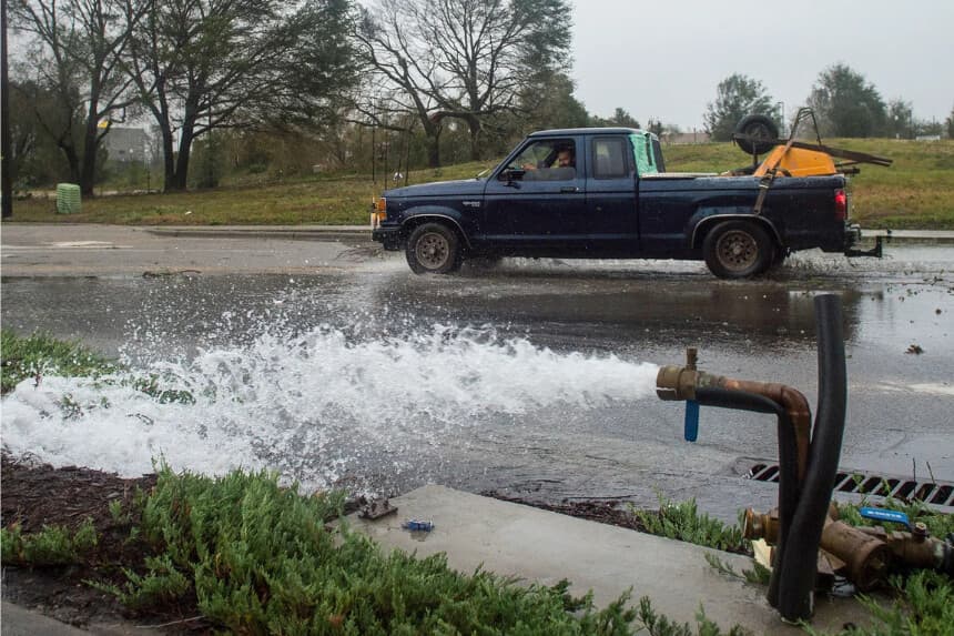 Un automóvil pasa por una tubería de agua rota dañada por fuertes vientos y fuertes lluvias del huracán Florence en Wilmington, Carolina del Norte, el 14 de septiembre de 2018. Según los expertos, reemplazar tuberías de agua viejas puede costar entre 1 y 4 millones de dólares por milla, dependiendo del tamaño de la tubería, la ubicación y el método de instalación. (Andrew Caballero-Reynolds/AFP vía Getty Images)