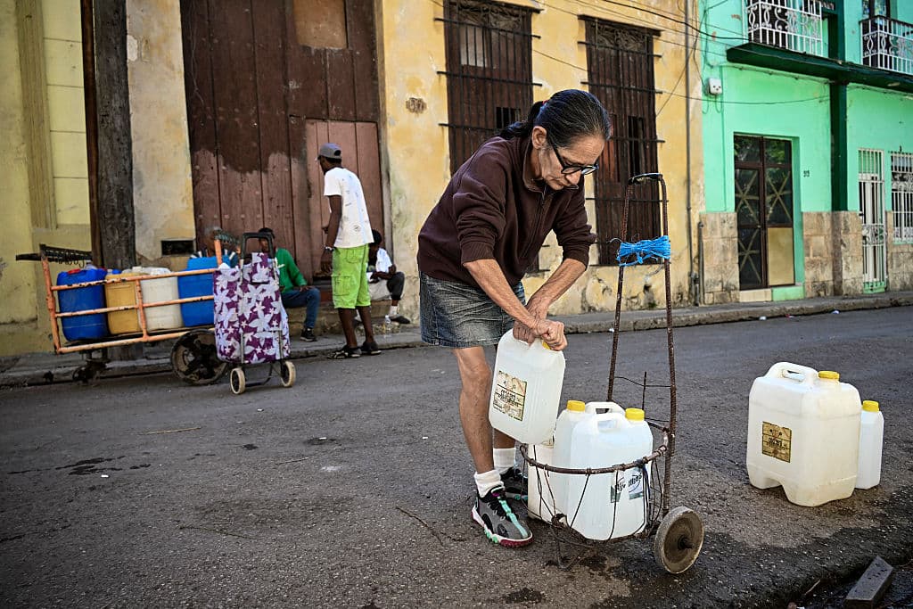 <em>Una mujer prepara su carrito tras llenar sus bidones de agua en La Habana durante un apagón nacional el 22 de marzo de 2026. Las autoridades cubanas se apresuraron ese día a restablecer el suministro eléctrico en la isla tras el segundo apagón nacional en menos de una semana, debido a las dificultades que atraviesa la red eléctrica por el envejecimiento de la infraestructura y el bloqueo petrolero estadounidense. (Foto de YAMIL LAGE / AFP vía Getty Images)</em>