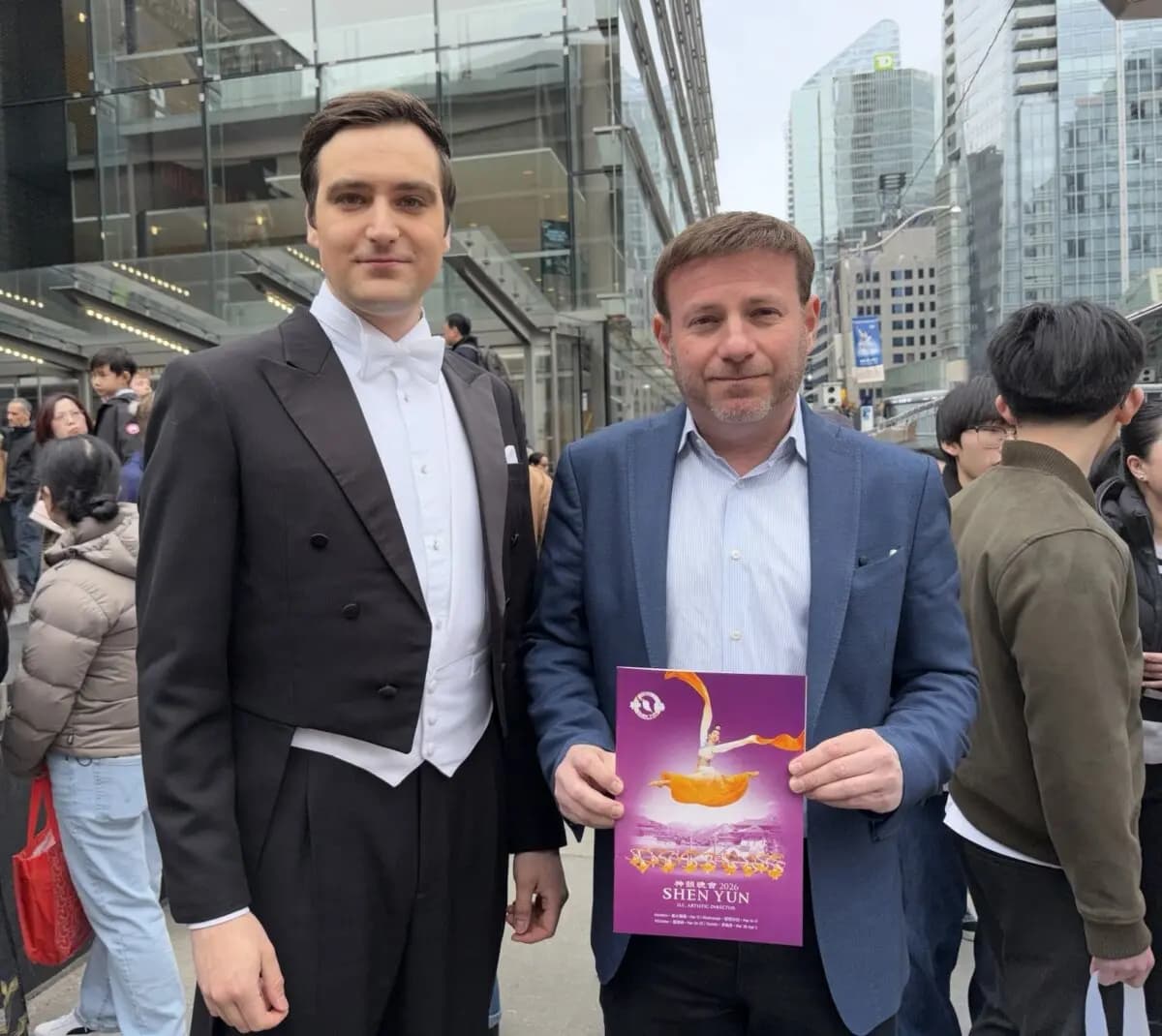 El diputado conservador Roman Baber sostiene un programa de Shen Yun junto a uno de los presentadores del espectáculo, frente al Four Seasons Centre for the Performing Arts de Toronto, el 29 de marzo de 2026. (The Epoch Times).