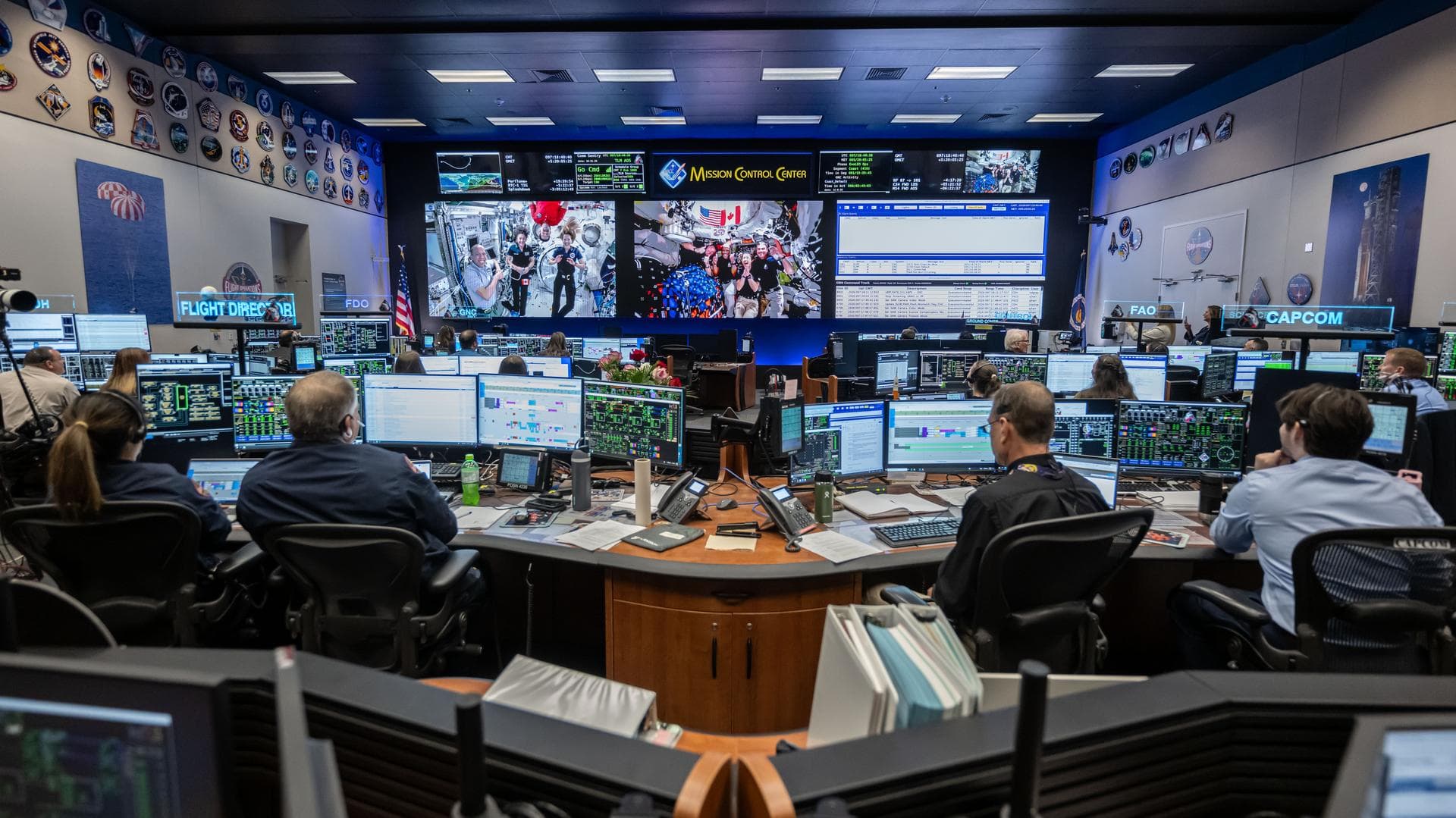 Los miembros de las tripulaciones de la Expedición 74 (izquierda) y Artemis II (derecha) de la Estación Espacial Internacional se ven a la vez en las pantallas dentro de la sala de control de vuelo de la Estación Espacial Internacional en el Control de Misión en el Centro Espacial Johnson de la NASA en Houston. Las dos tripulaciones se conectaron en una llamada de barco a barco de 15 minutos el 7 de abril de 2026, mientras la tripulación del Artemis II regresaba de la Luna. ( ROBERT MARKOWITZ NASA-JSC/NASA)