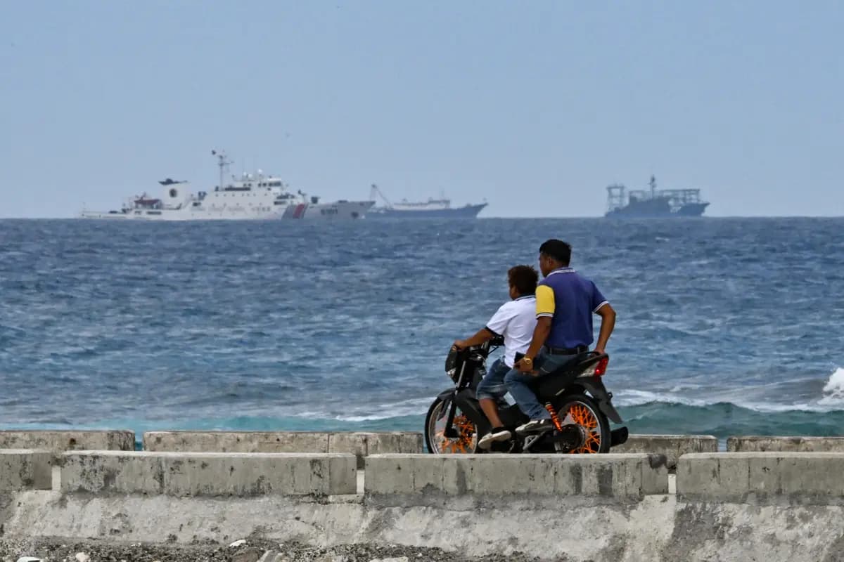 <em>Se observa un buque de la Guardia Costera de China mientras  motociclistas circulan en la isla Thitu, en el Mar de China Meridional, el 21 de febrero de 2026. (Jam Sta Rosa/AFP vía Getty Images)</em>