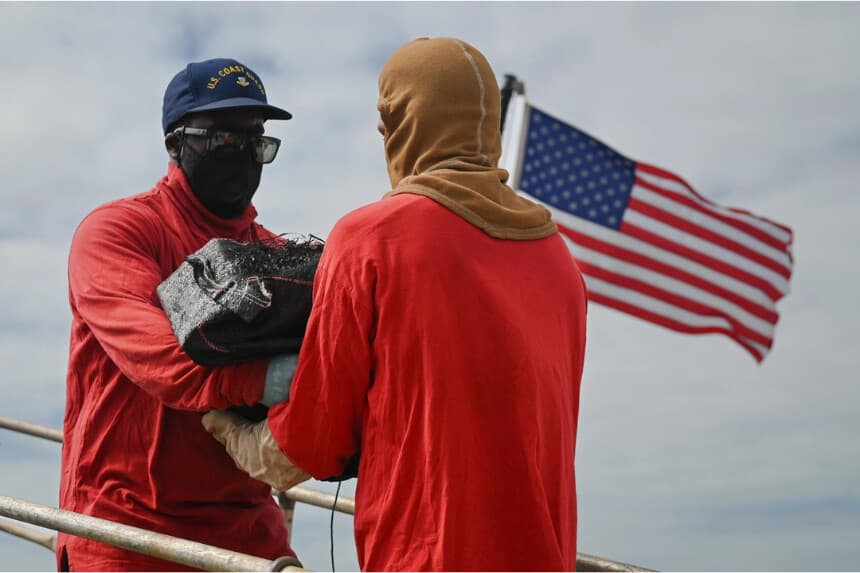 Dos miembros de la tripulación del Coast Guard Cutter Tampa pasan un fardo de cocaína durante una descarga de drogas en la Base Miami Beach el 16 de abril de 2026. (Cortesía de los EE.UU. Guardia Costera)