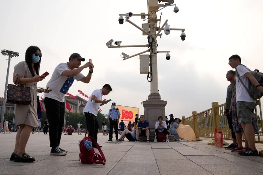 Un policía vigila junto a unas cámaras de vigilancia mientras la gente toma fotos en la plaza de Tiananmen, en Pekín, el 15 de julio de 2021. (Foto AP/Ng Han Guan)