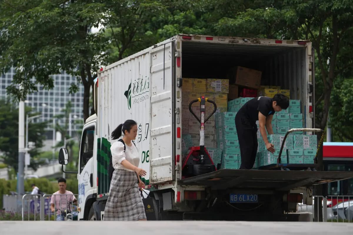 Una mujer pasa junto a un trabajador que descarga cajas de bebidas de un camión en el distrito comercial de Shenzhen Bay, en Shenzhen (provincia de Guangdong, China), el 19 de septiembre de 2025. (Andy Wong/AP Photo).