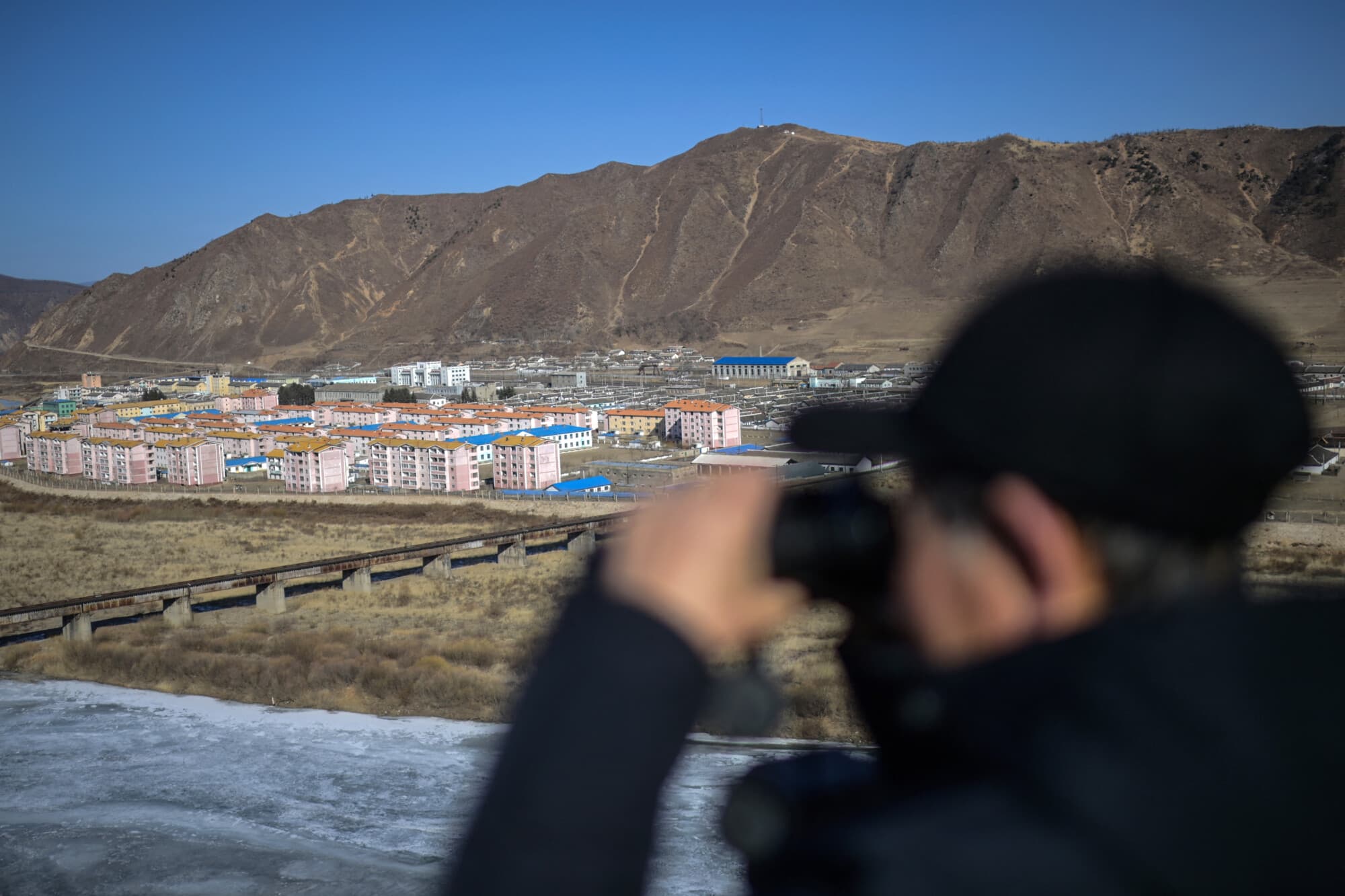 Esta fotografía, tomada el 26 de febrero de 2024, muestra a un hombre que observa con unos binoculares la ciudad norcoreana de Namyang desde la ciudad de Tumen, en la provincia de Jilin, al noreste de China. (Foto de PEDRO PARDO/AFP vía Getty Images)