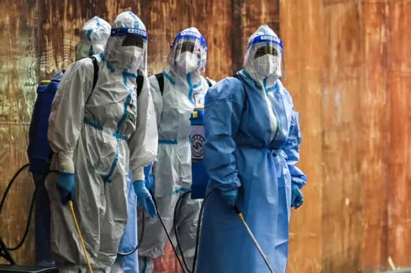 El 4 de junio de 2022, unos trabajadores que manipulan desinfectante observan junto a una zona residencial sometida a un confinamiento por COVID-19 en el distrito de Huangpu, en Shanghái. (Héctor Retamal/AFP vía Getty Images).