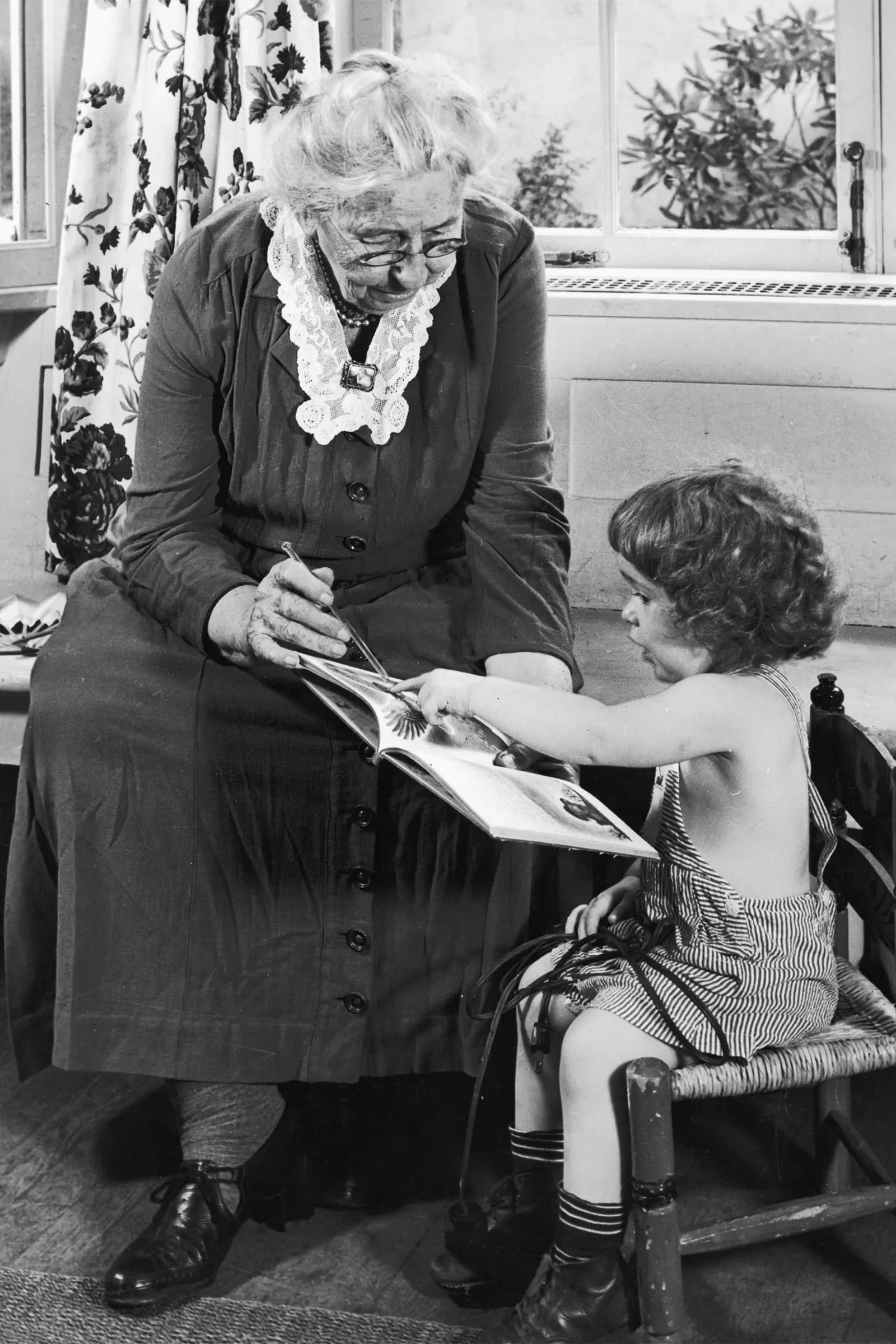 <em>Una abuela se sienta con su nieta pequeña, señalando una imagen en un libro de cuentos mientras la niña sigue la lectura, década de 1940. (Foto de Frederic Hamilton/Hulton Archive/Getty Images).</em>
