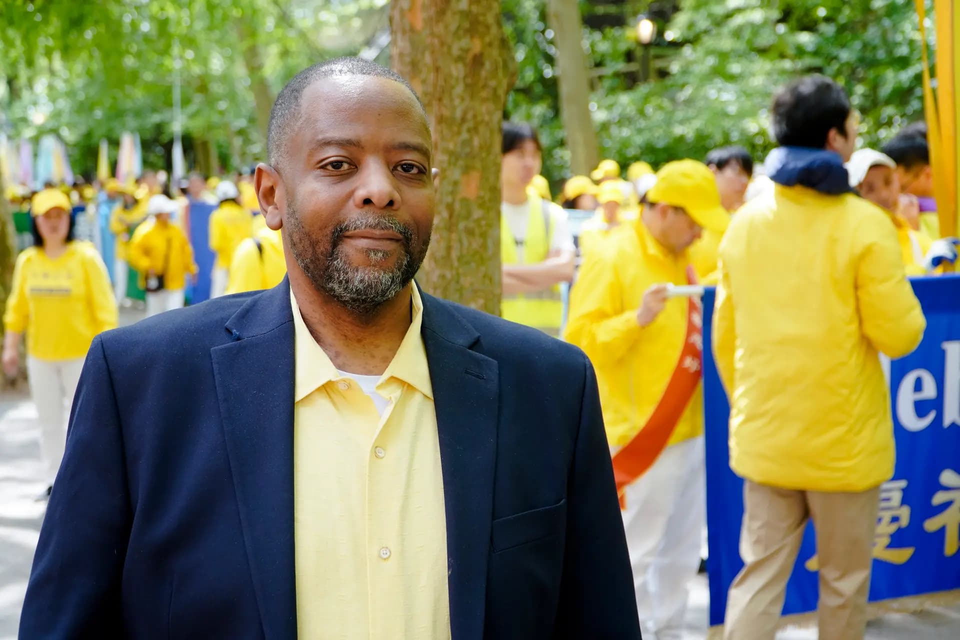 <em>Lawrence Rweyemamu, de 50 años, practica Falun Gong desde 2009. Se encuentra en la plaza Dag Hammarskjöld, donde los practicantes de Falun Gong se preparan para un desfile que celebra el Día Mundial de Falun Dafa, el 13 de mayo de 2026. (Nicholas Zifcak/The Epoch Times).</em>