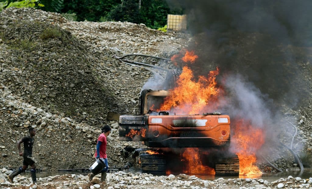 <em>Lugareños intentan extinguir el fuego en la maquinaria pesada destruida por las fuerzas armadas durante una operación en una mina de oro ilegal en Triángulo de Telembi, Colombia, el 25 de enero de 2023. Desde un helicóptero del ejército que sobrevolaba la zona, las fuerzas de seguridad colombianas divisaron varias minas de oro ilegales en la selva. Las fuerzas armadas aterrizaron repentinamente y se encontraron con trabajadores enfurecidos, pero los repelieron y destruyeron la maquinaria utilizada para extraer el oro. La operación representa un duro golpe a la minería ilegal y una ofensiva contra los grupos armados que se lucran con las minas ilícitas en este país asolado por el conflicto. (Foto de DANIEL MUNOZ/AFP vía Getty Images)</em>