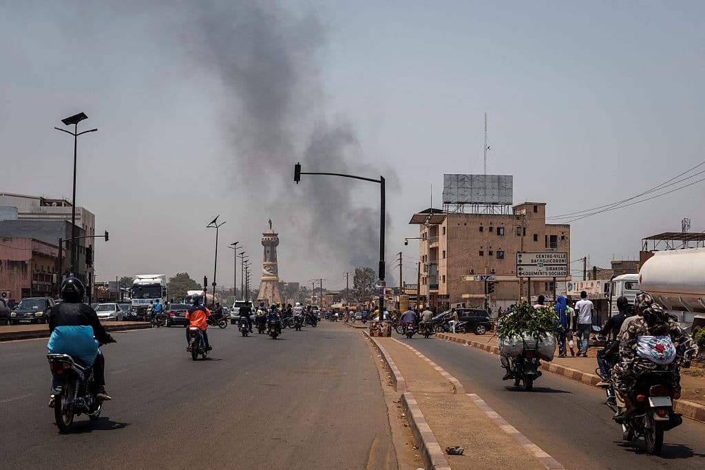 <em>Una columna de humo negro se eleva sobre los edificios mientras el tráfico pasa junto al monumento de la Torre África en Bamako el 26 de abril de 2026. Los ataques sorpresa del 25 de abril de 2026, sincronizados por los rebeldes tuareg de la coalición Frente de Liberación de Azawad (FLA) y el grupo yihadista Grupo de Apoyo al Islam y los Musulmanes (JNIM), tuvieron como objetivo varias zonas del vasto país árido. Los combates se reanudaron el 26 de abril en varias zonas, incluidas Kita, cerca de Bamako, Kidal, Gao y Severe. Mientras tanto, los rebeldes tuareg anunciaron un acuerdo que permitía a las fuerzas rusas que apoyaban al ejército de Malí retirarse de la ciudad norteña de Kidal, que, según afirmaban, estaba "totalmente" bajo su control. (Foto de AFP vía Getty Images)</em>