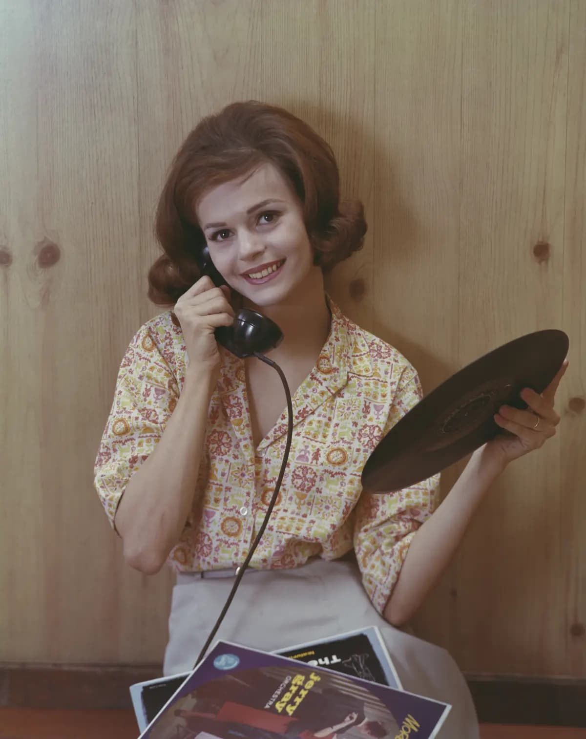 <em>Una joven realiza una llamada telefónica mientras sostiene un disco de la Jerry Gray Orchestra, alrededor de 1955. Las décadas de 1950 y 1960 suelen considerarse la época dorada de los discos de vinilo. (Archive Photos/Getty Images).</em>