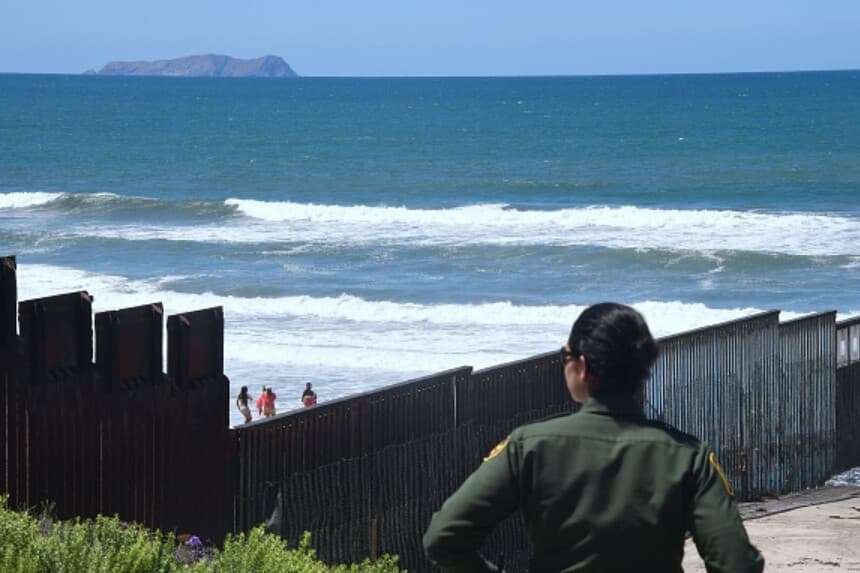 Imagen Ilustrativa: Un agente de la Oficina de Aduanas y Protección Fronteriza de EE. UU. vigila cerca de la estructura fronteriza que se adentra en el Océano Pacífico en San Diego, California, el 17 de abril de 2018, mientras personas visitan la playa en La Playa, México. La imagen fue tomada un día después de que California rechazara el despliegue de tropas de la Guardia Nacional en la frontera. (Frederic J. Brown / AFP vía Getty Images).