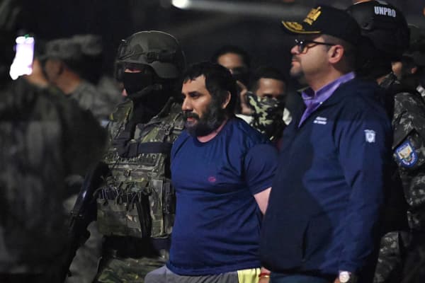 <em>El narcotraficante José Adolfo Macías, alias “Fito”, es custodiado por militares y por el ministro del Interior de Ecuador, John Reimberg, tras su llegada a la base aérea de Guayaquil el 25 de junio de 2025, luego de ser recapturado en Manta. La fuga de “Fito” en enero de 2024 desató una de las peores olas de violencia en la historia reciente del país. (Foto de Marcos PIN/AFP vía Getty Images)</em>