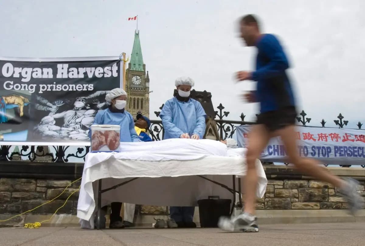 Un hombre pasa corriendo junto a unos practicantes de Falun Gong que utilizan una recreación de la sustracción de órganos como parte de su protesta contra China y la persecución que esta ejerce sobre los practicantes de Falun Gong, en la Colina del Parlamento de Ottawa, el 2 de mayo de 2008. (The Canadian Press/Tom Hanson)